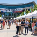 A bustling crowd of families and corporate groups browsing white art vendor tents at the Utah Arts Festival in front of the Salt Lake City Public Library.